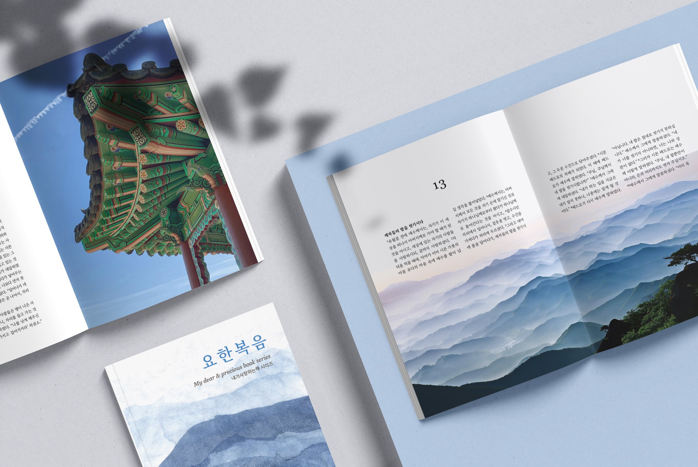 요한복음 cover and two open interior spreads, a Korean pavilion roof and misty blue mountains, on a pale blue flat-lay