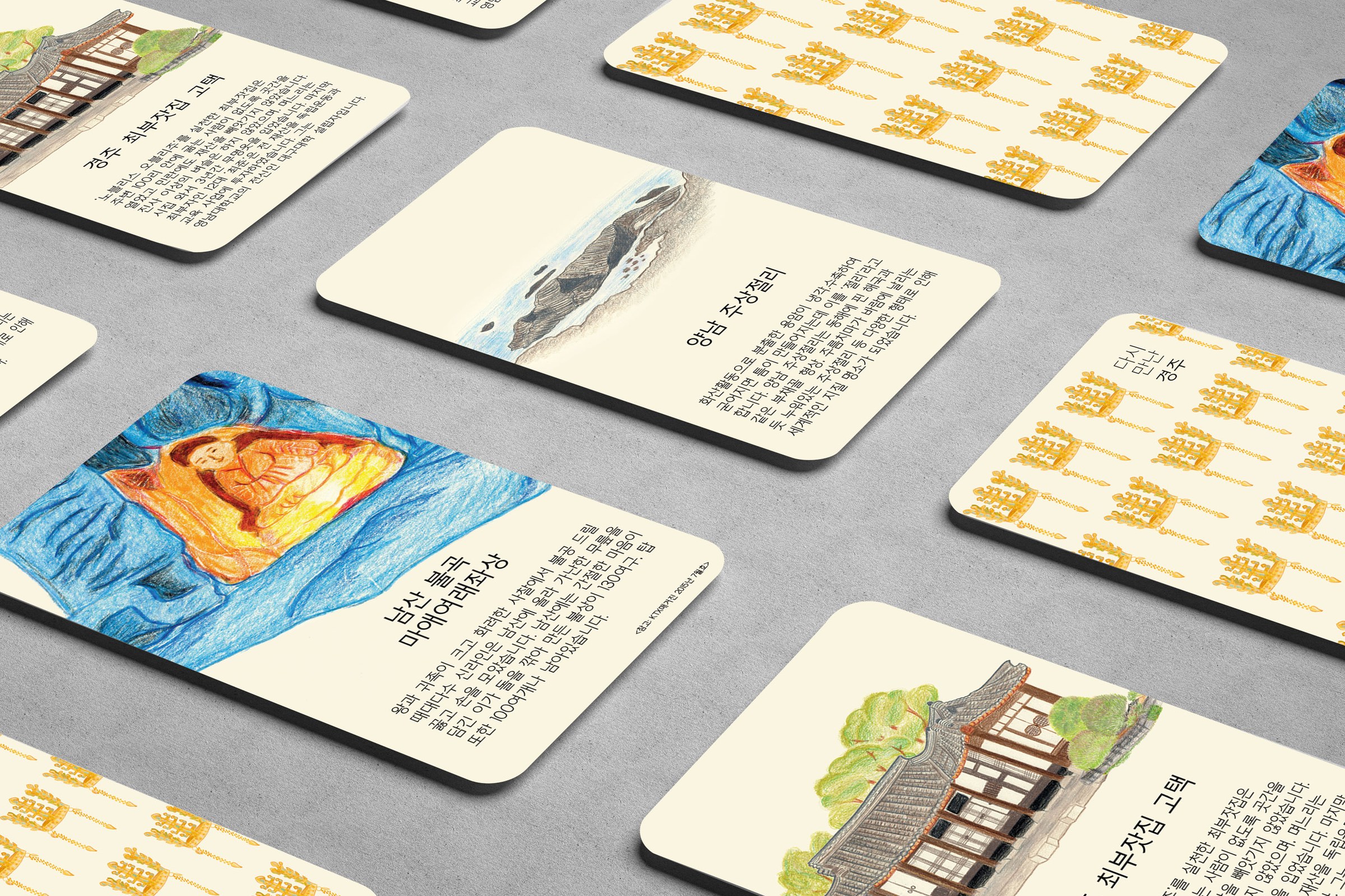 A grid of rounded cream landmark cards seen at an angle on a grey surface: each card pairs a coloured-pencil drawing with a Korean heading and short text: the Choebuja house, Yangnam Jusangjeolli and the Namsan rock-carved Buddha, alternating with cards patterned with golden crowns